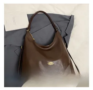 Detail view of coffee brown crescent tote with gold handmade metal plaque and straps
