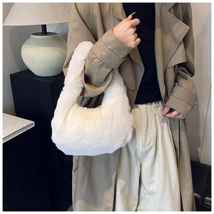 Detail view of a white plush faux fur dumpling handbag worn as an armpit bag for winter