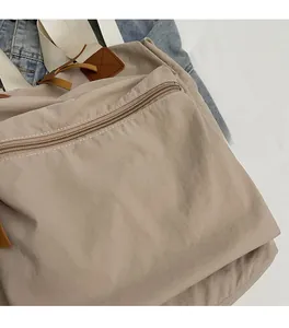 Close-up of soft beige nylon tote bag fabric and front metal zipper pocket detail