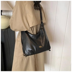 Close-up of a large black leather tote bag worn by a model in a beige trench coat