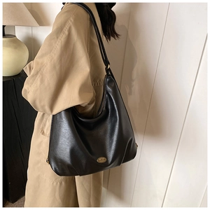 Detail of elegant black leather hobo bag featuring polished gold metal logo hardware