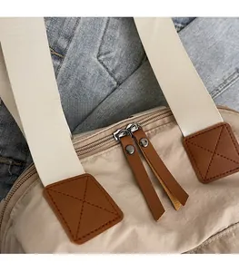 Detail of smooth two-way metal zippers and brown leather pulls on a beige canvas bag