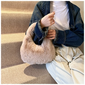 Close-up of the soft plush texture and curved handle on this beige faux fur dumpling bag