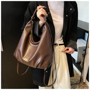 Detail of soft dark brown matte leather hobo bag featuring an oval golden metal logo