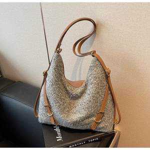 Detail der grauen Strick-Tweed-Hobo-Tasche mit braunen Lederriemen auf Sofa