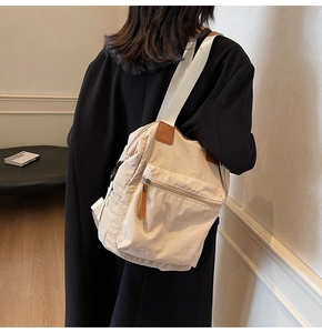 Side view of beige nylon shoulder bag with wide strap and brown leather zipper pull