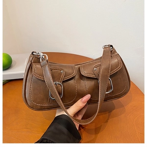 Detailed view of brown leather shoulder bag with double pockets and silver metal buckles