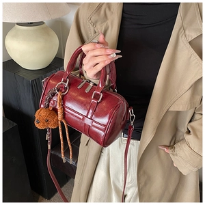 Close-up of wine red Boston bag with shiny leather, woven detail and plush bear charm