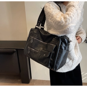 Détails d'un sac de voyage en similicuir noir avec zips argentés porté sur un pull