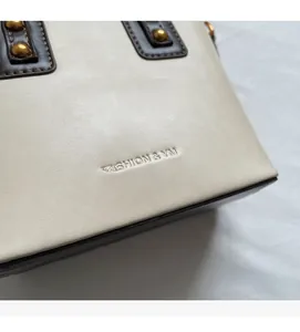 Détail du sac en cuir crème avec bordure marron, rivets dorés et logo en relief