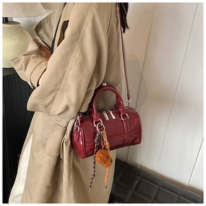 Détail du sac Boston bordeaux avec pendentif ours et texture en cuir brillant