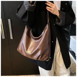 Detail of vintage brown leather tote bag with gold logo plaque on a shoulder strap