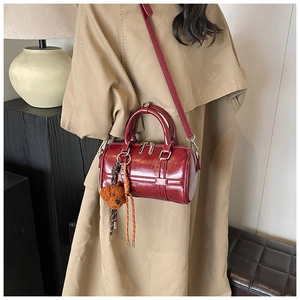 Détail d'un sac Boston en cuir bordeaux avec un charmant accessoire chiot en peluche