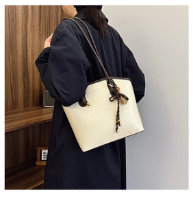 Detail view of cream tote bag with brown leather straps and woven knot ornament