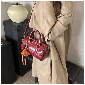 Detail of dark red cylinder bowling bag with plush charm and silver metal hardware