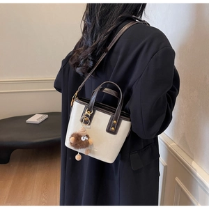 Détail du sac seau crème avec bordure marron, logo et breloque ours sur le mannequin