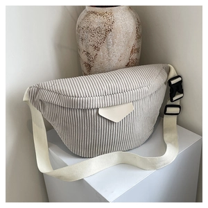 Détail du sac banane en velours côtelé gris clair avec sangle en toile sur un socle