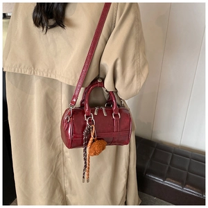Détail du sac Boston bordeaux brillant avec pompon porté sur un trench-coat crème élégant