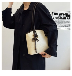 Close-up of cream tote bag with dark brown edges and braided charm hanging on a shoulder