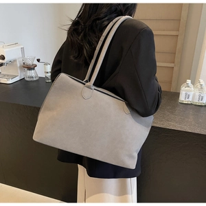 Detail view of a large grey suede tote bag worn on shoulder in a modern cafe setting