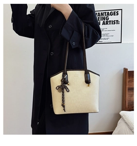 Detail of a beige tote bag showing high-quality leather texture and woven charm accessory