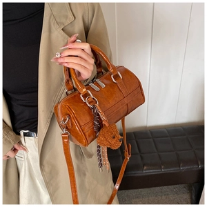 Détail d'un sac Boston marron avec texture cuir, doubles poignées et breloque ourson
