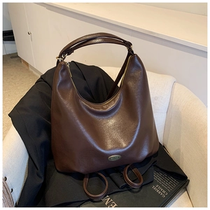 Detail of vintage dark brown leather hobo bag on suit with metal logo plaque