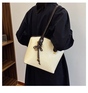 Detail view of cream tote bag with dark brown trim and woven knot charm on a shoulder strap