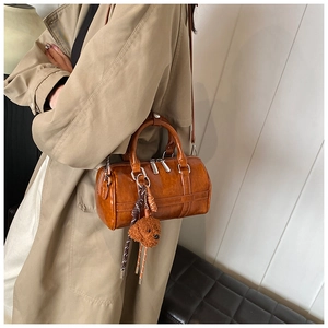 Sac Boston marron avec charm nounours porté par un mannequin en trench-coat kaki chic