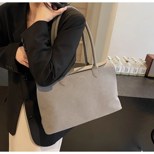 Close-up of a large grey suede tote bag worn on shoulder in a minimalist setting
