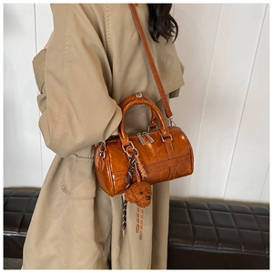 Sac Boston vintage marron porté en bandoulière sur un trench avec pendentif ours