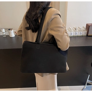 Detail of a large black matte leather tote bag worn by a model in an elegant cafe setting