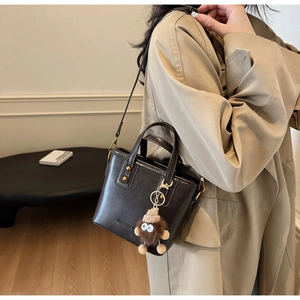 Détail d'un sac seau bandoulière marron foncé avec rivets et breloque peluche