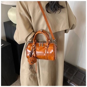Retro brown cylinder Boston bag with plush bear charm shown in a lifestyle side view