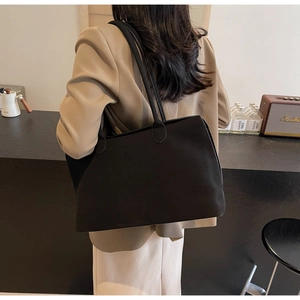 Close-up of a large black tote bag in felt texture on a model wearing a beige blazer
