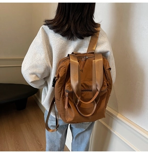 Brown nylon backpack worn by model in a minimalist room showing back view and fit