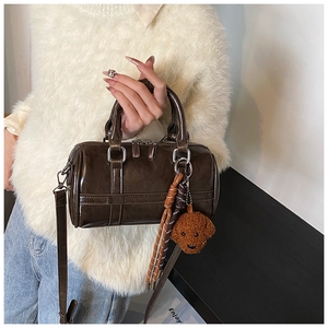Detail of dark brown glossy Boston bag with teddy dog charm and adjustable strap