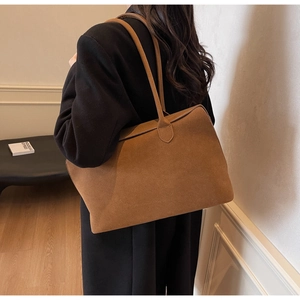 Caramel brown suede tote bag shown on shoulder in a minimalist indoor setting
