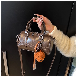 Close-up of a dark brown glossy PU leather Boston bag with a cute puppy plush charm