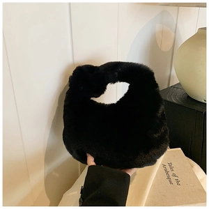 Detail view of a black faux fur plush handbag held against a minimalist chic background
