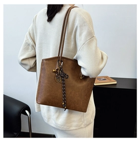 Detail of dark brown vintage tote bag with woven knot and golden racket charm accessory