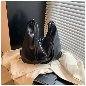 Close-up of black glossy hobo bag with metal zipper on beige blazer and book