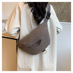 Vue détaillée d'un sac bandoulière en velours côtelé marron porté sur un manteau beige