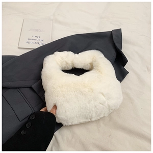 Top view of a soft white faux fur dumpling handbag on a grey suit jacket background