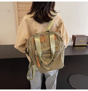 Detail of sage green canvas backpack with leather accents worn by a person from the back