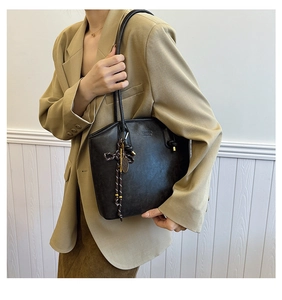 Detail view of black vintage leather tote bag with woven rope charm and metallic accents