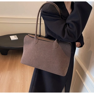 Detail of a large brown suede tote bag featuring slim shoulder straps and a flap closure
