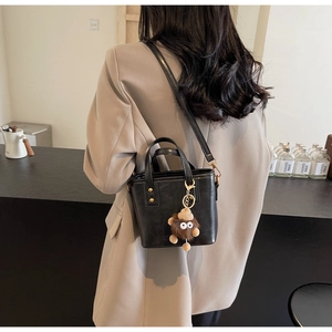 Détail d'un sac seau noir mat avec rivets dorés et charmant pendentif monstre en peluche
