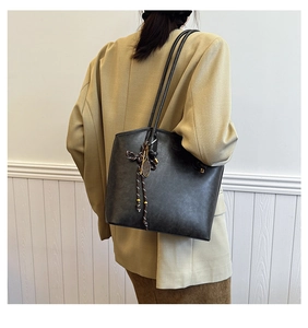 Detailed view of black vintage tote bag with woven charm on a beige blazer outfit
