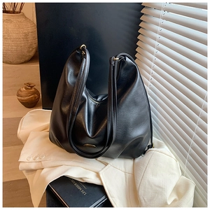 Close-up of elegant black leather Hobo bag with metal logo on white blazer background